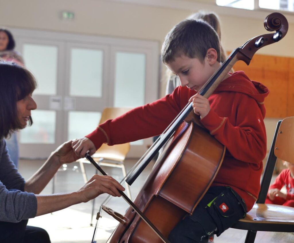 Ein Kind spielt Cello unter Anleitung der Cellolehrerin