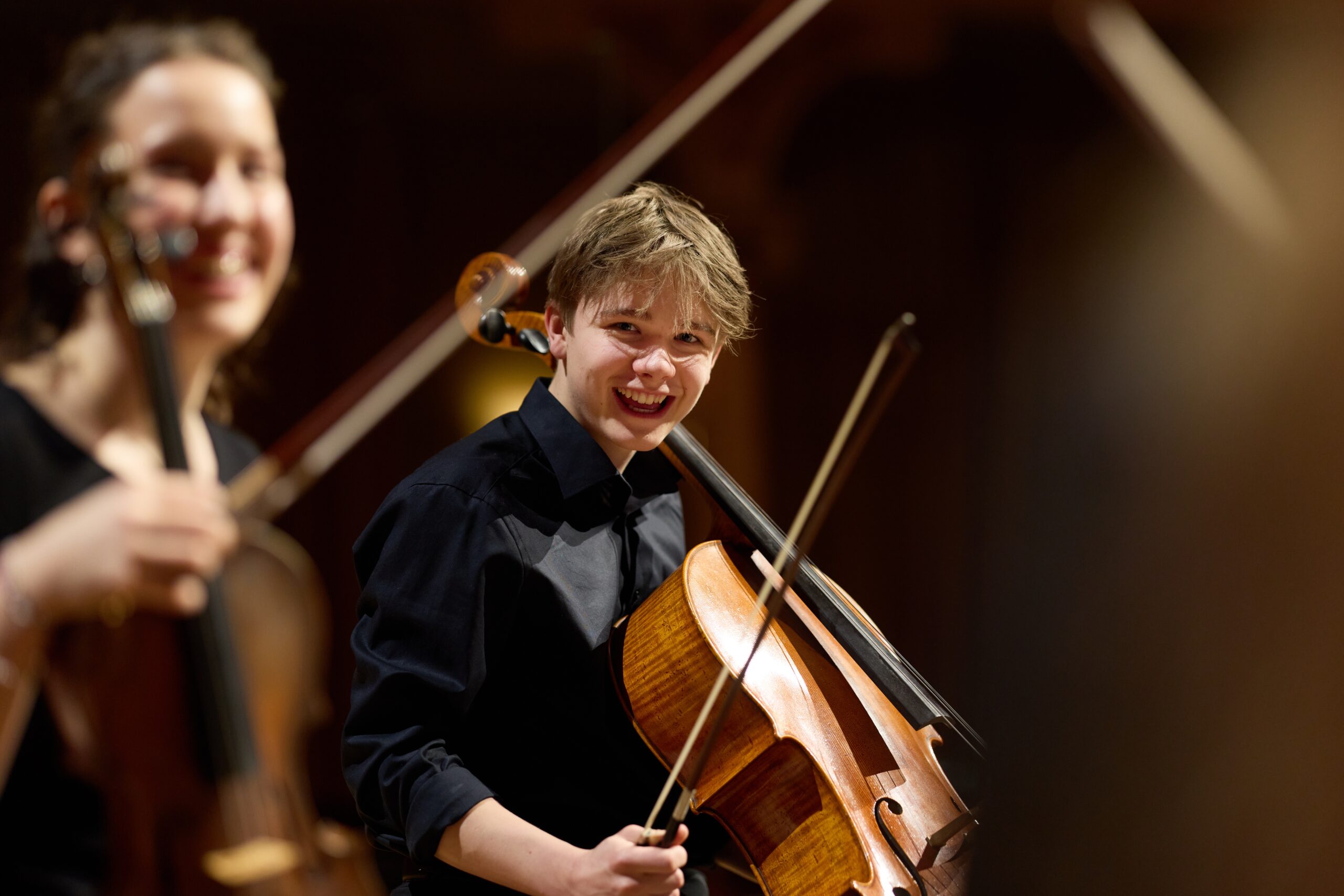 Juge Musiker:innen in dunkler Kleidung mit Streichinstrumenten, die in die Kamera lächeln.