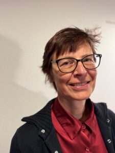 Lächelnde Frau mit kurzer brauner Frisur und Brille vor neutralem Hintergrund