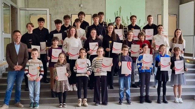 Musikschülerinnen und -schüler halten Urkunden auf einer Treppe.