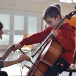 Ein Kind spielt Cello unter Anleitung der Cellolehrerin